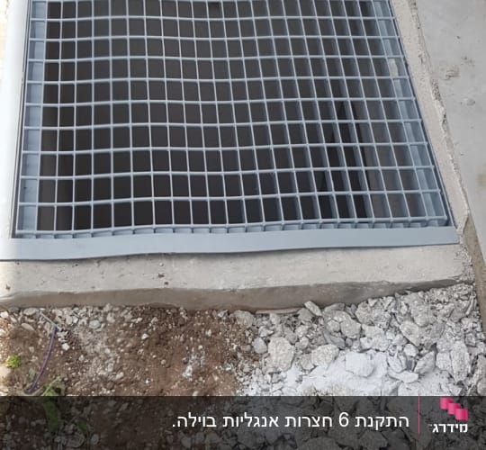 סבכת מתכת אפורה מותקנת מעל פתח חצר אנגלית באתר בנייה